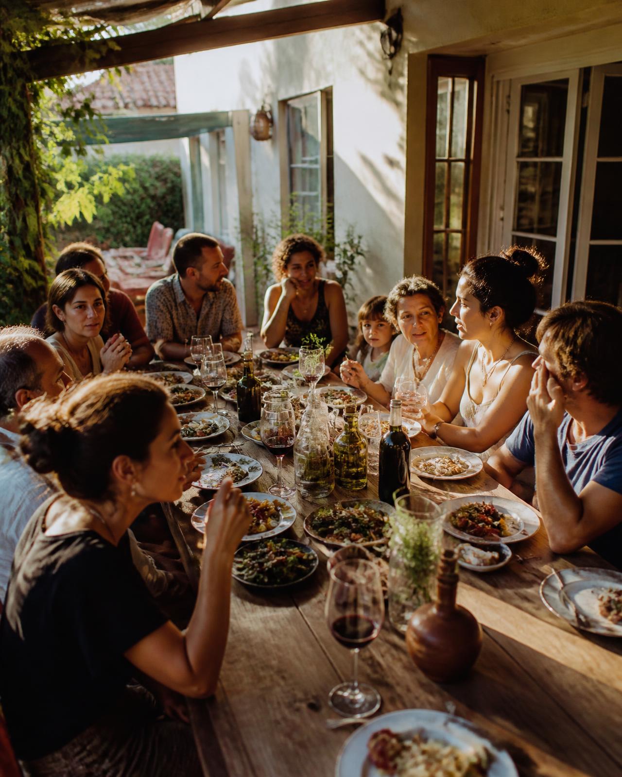 A family and friends crowded around a long table on a sunlit patio